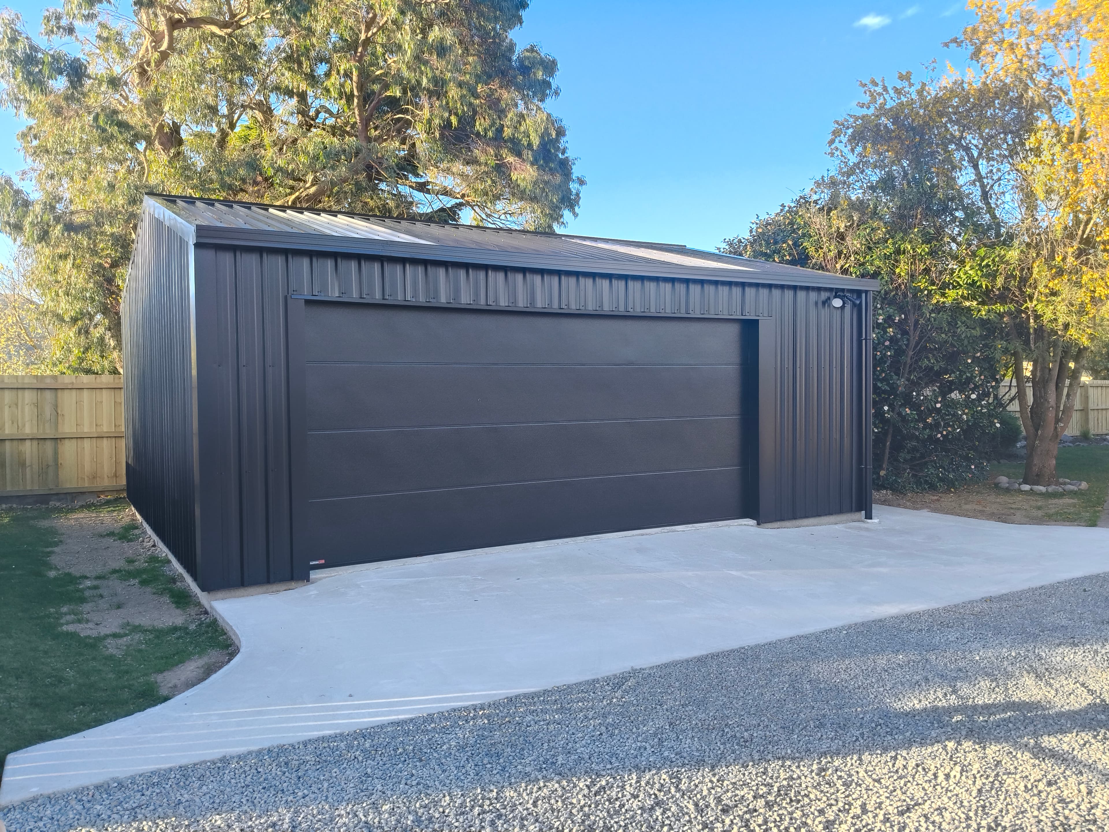 Modern black corrugated metal garage with a wide sectional door on a concrete driveway.